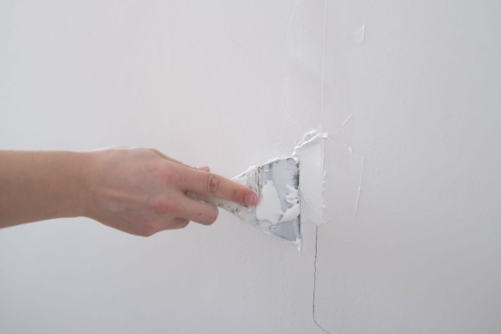 Close-up of a hand performing drywall services, repairing a wall by applying joint compound to a crack.